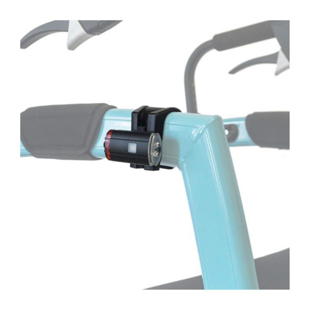 A close-up of a compact Rollz Motion Rollator Accessory, a black and red bicycle light, is attached to a light blue handlebar with a black strap. It blends into an adventurous journeys vibe, with a blurred background hinting at essential wheelchair gear for explorers.